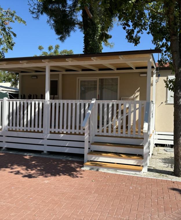 Casetta con veranda e giardino, circondata da alberi e mattoni rossi.