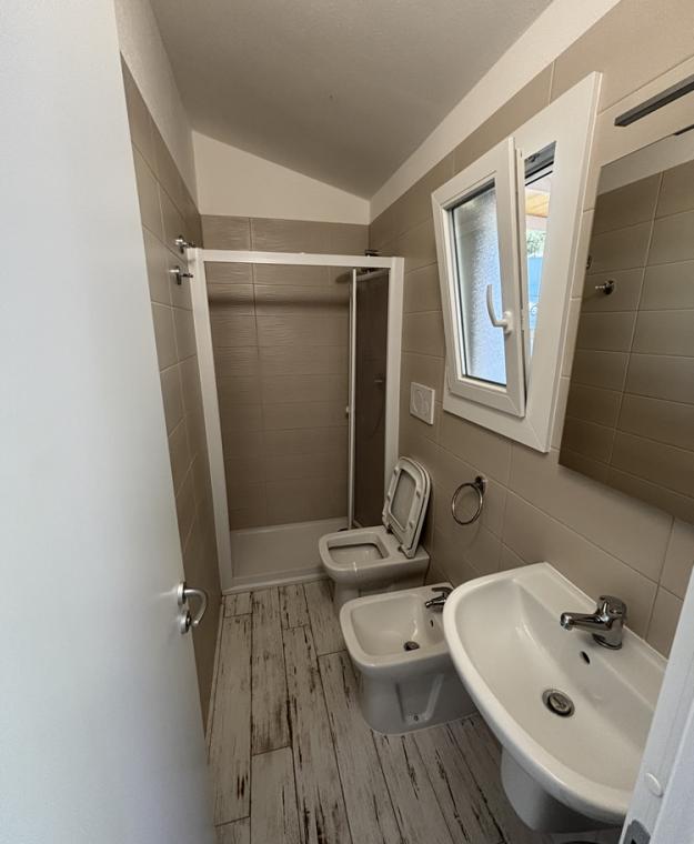 Bagno moderno con doccia, bidet e lavabo, pavimento effetto legno.